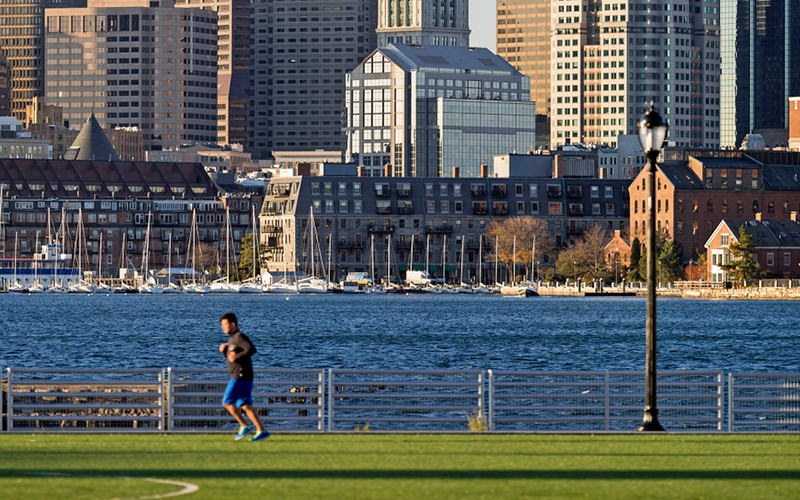 man takes a morning run alongside the water with Boston in the background